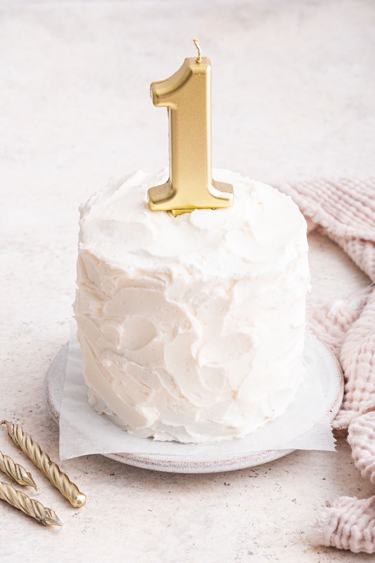 A frosted smash cake with a one candle on top.