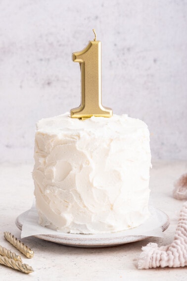 A frosted smash cake with a one candle on top.