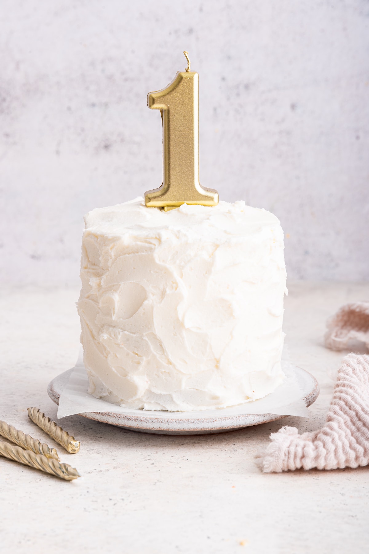 A frosted smash cake with a one candle on top.