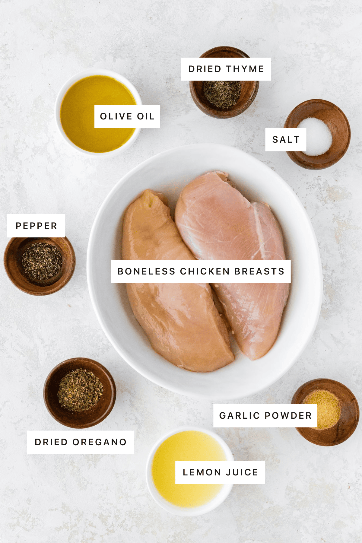 Ingredients measured out to make Easy Grilled Chicken Breast: olive oil, thyme, salt, pepper, chicken breasts, oregano, garlic powder and lemon juice.