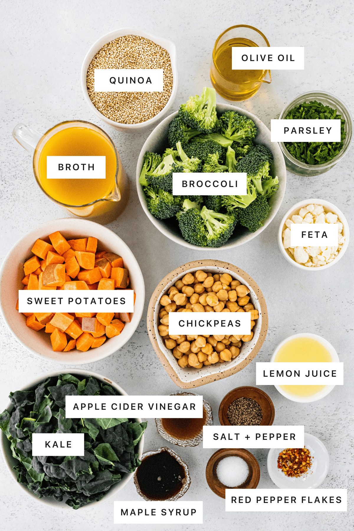 Ingredients measured out to make Roasted Broccoli Quinoa Salad: quinoa, olive oil, parsley, broth, broccoli, feta, sweet potatoes, chickpeas, lemon juice, vinegar, kale, salt, pepper, maple syrup and red pepper flakes.