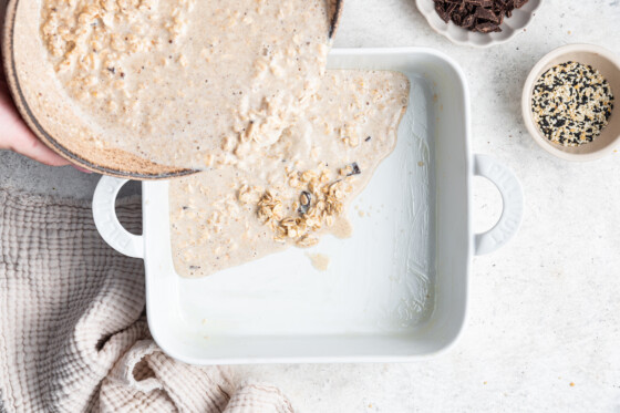 Tahini baked oatmeal mixture being poured into a prepared square baking dish.