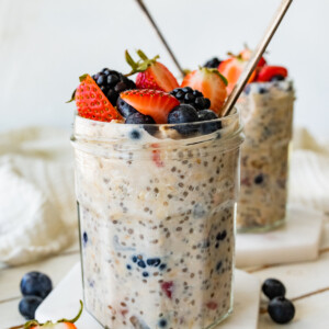 Two mason jars with cottage cheese overnight oats with metal spoons and topped with fresh berries.