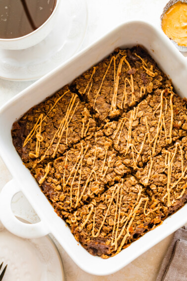 Coffee baked oatmeal sliced in a square baking dish and topped with a drizzle of nut butter.