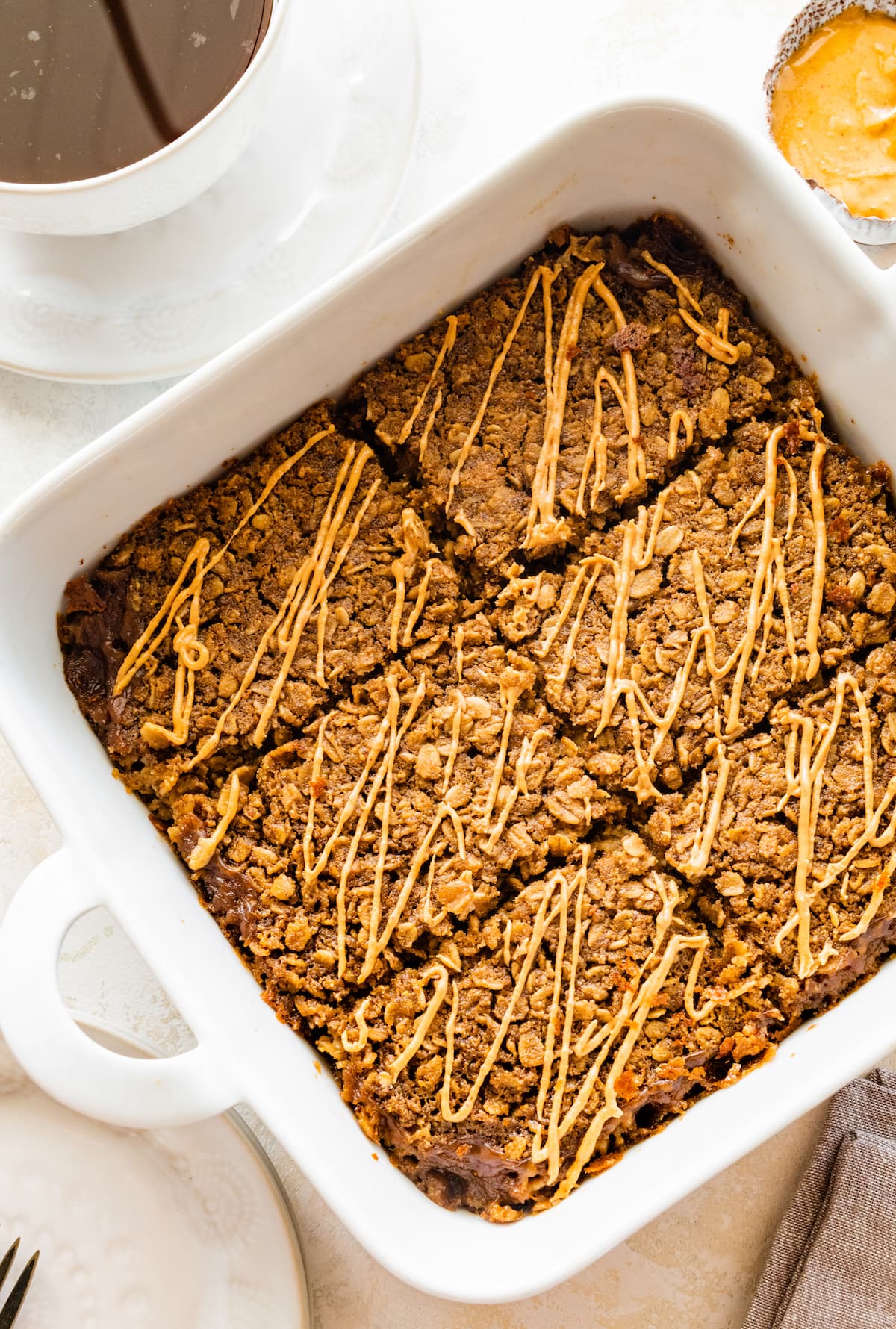 Coffee baked oatmeal sliced in a square baking dish and topped with a drizzle of nut butter.