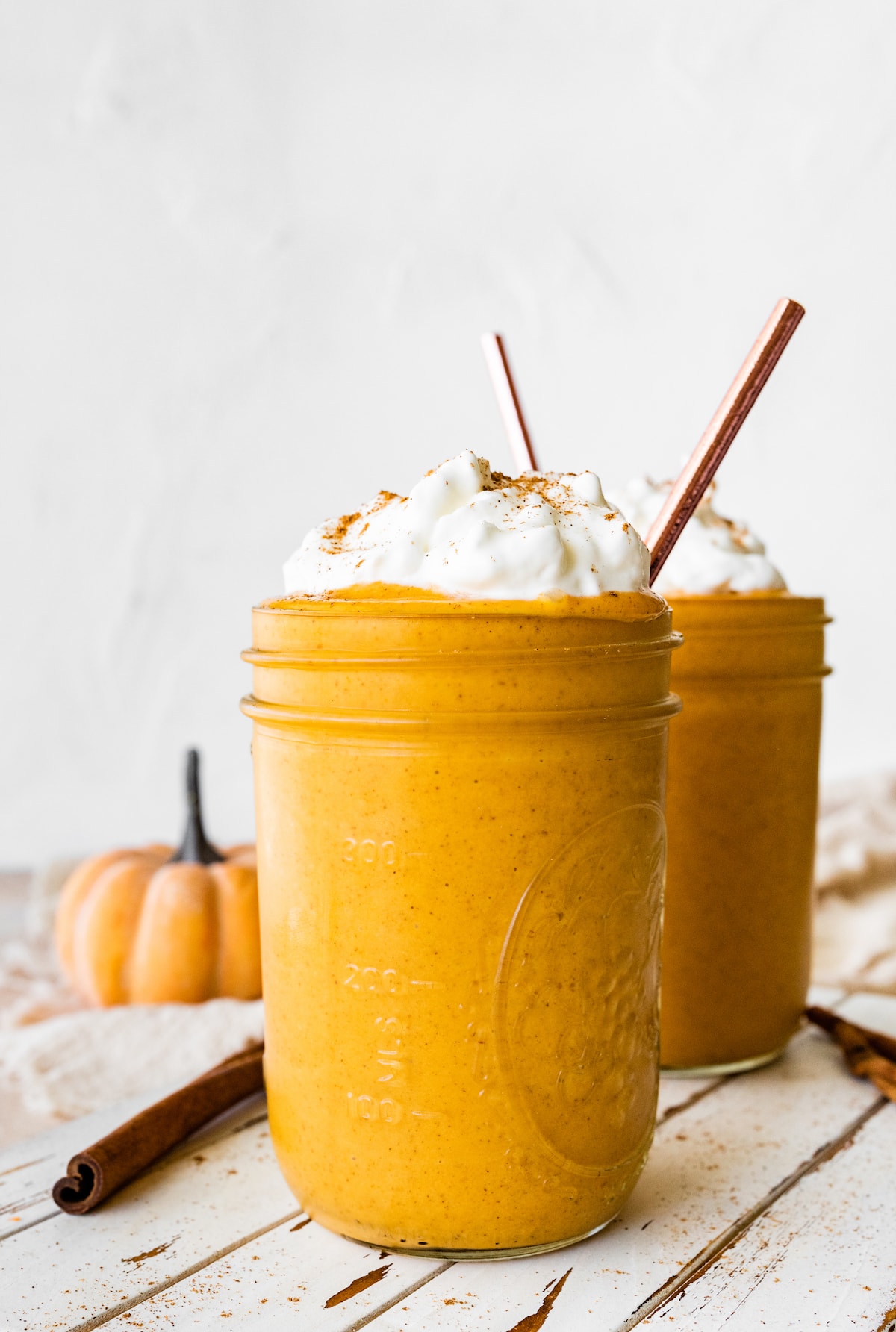 Two glass mason jars with pumpkin protein shakes topped with whipped cream and ground cinnamon.