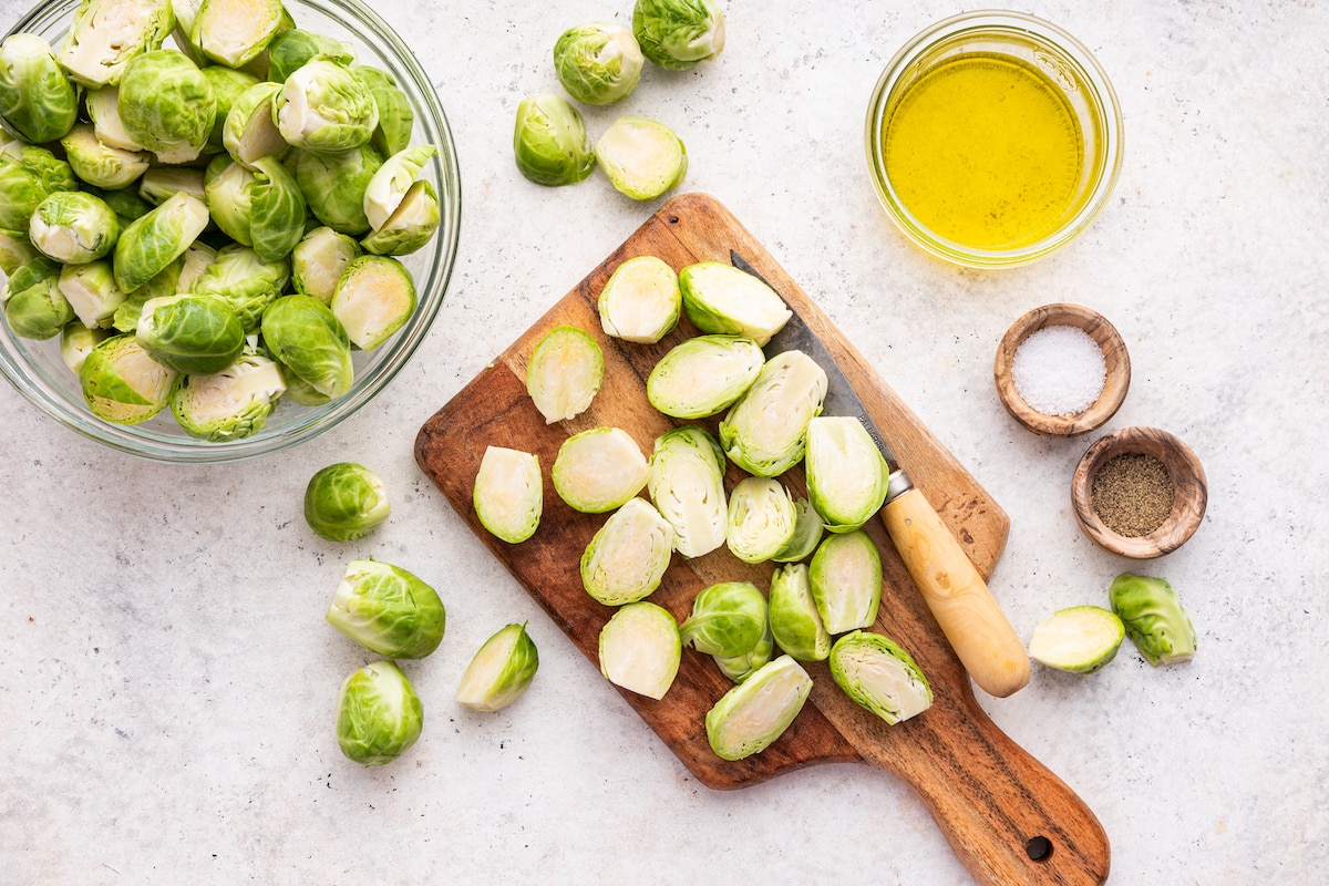 Brussels sprouts on a small wooden cutting board sliced in half with a small kitchen knife.