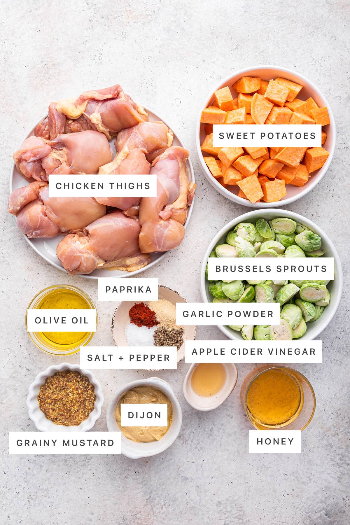 Ingredients measured out to make a Honey Mustard Chicken Sheet Pan Meal: chicken thighs, sweet potatoes, brussels sprouts, paprika, garlic powder, olive oil, salt, pepper, vinegar, grainy mustard, dijon and honey.