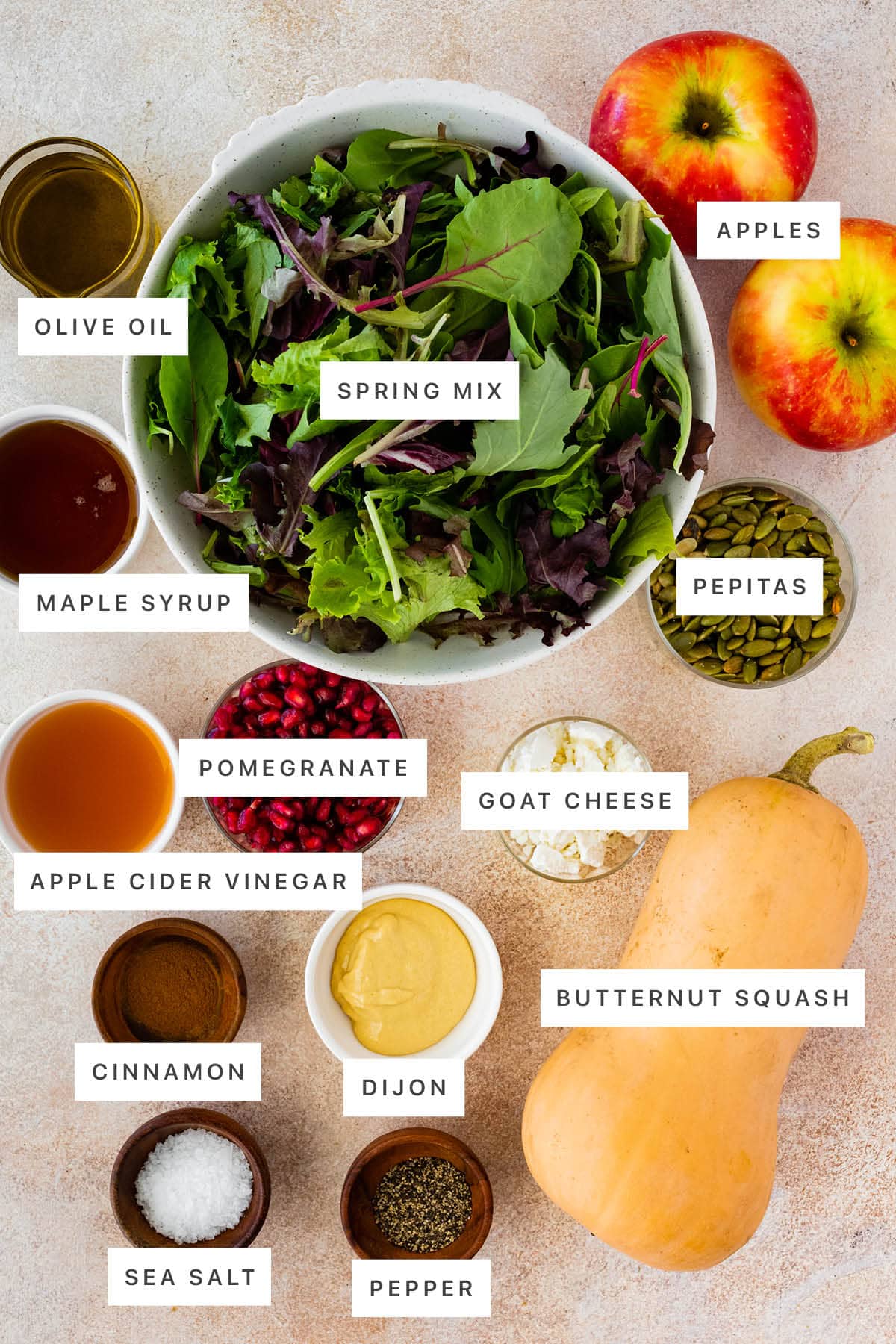 Ingredients measured out to make Thanksgiving Salad: olive oil, spring mix, apples, maple syrup, pepitas, pomegranate, goat cheese, vinegar, cinnamon, dijon, butternut squash, sea salt and pepper.