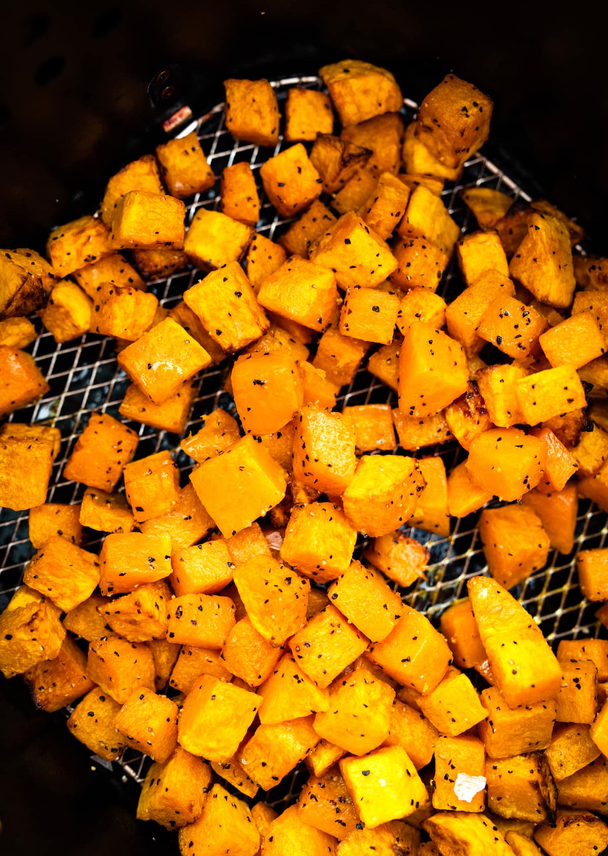Cubed butternut squash Cubed butternut squash that has been seasoned and is sitting in an air fryer basket in an air fryer.