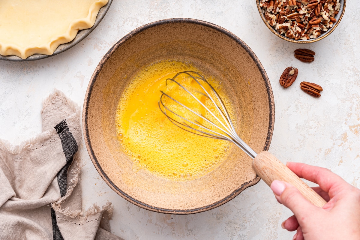 A woman's hand whisking the eggs in a mixing bowl for the pecan pie.