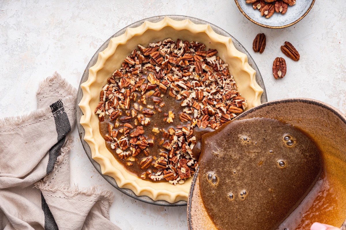 The pecan pie filling being poured over the chopped pecans in the pie crust.