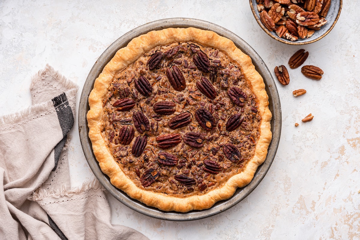 Uncut pecan pie in a pie dish with pecan halves on top.