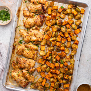 A large sheet pan with cooked honey mustard chicken, roasted sweet potatoes, and Brussels sprouts.