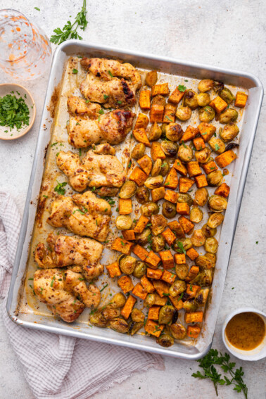 A large sheet pan with cooked honey mustard chicken, roasted sweet potatoes, and Brussels sprouts.
