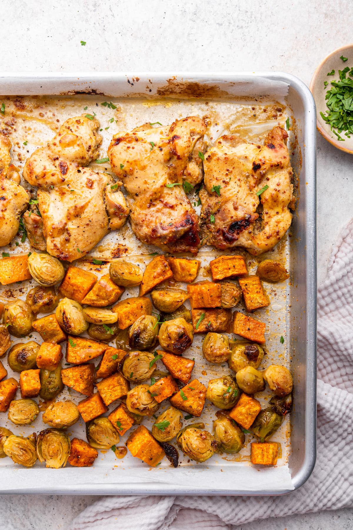 A sheet pan with cooked chicken along with roasted sweet potato and Brussels sprouts.