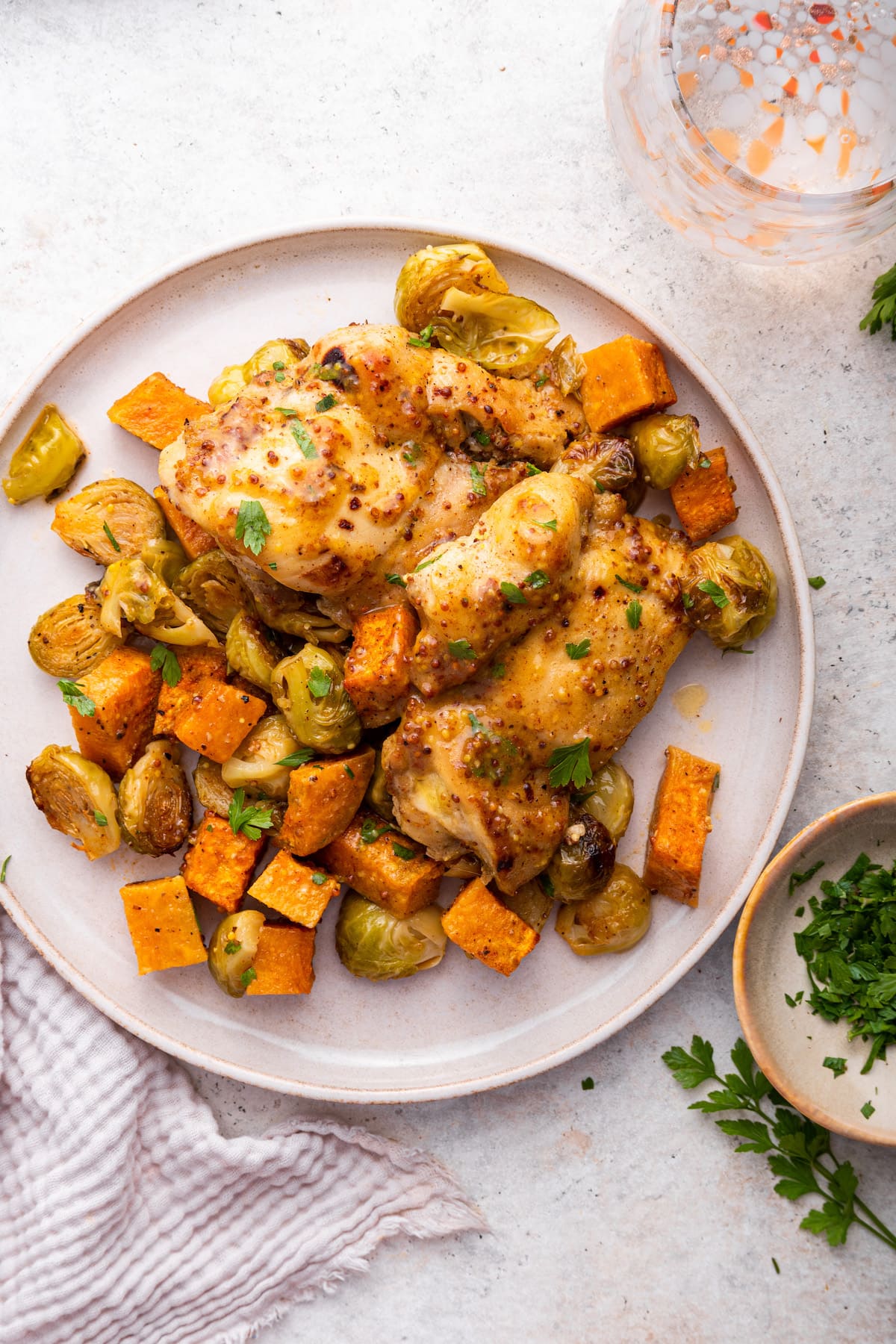 A serving of honey mustard chicken on a plate with roasted sweet potatoes and Brussels sprouts.