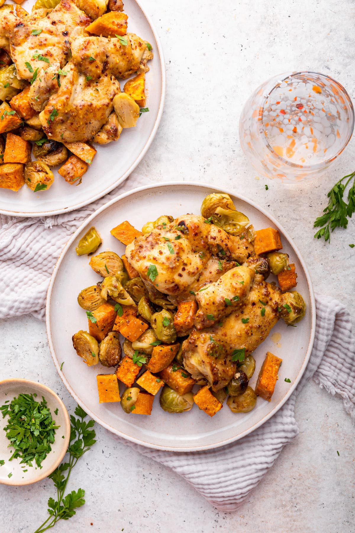A serving of roasted chicken on a plate with diced sweet potato and brussels sprouts.