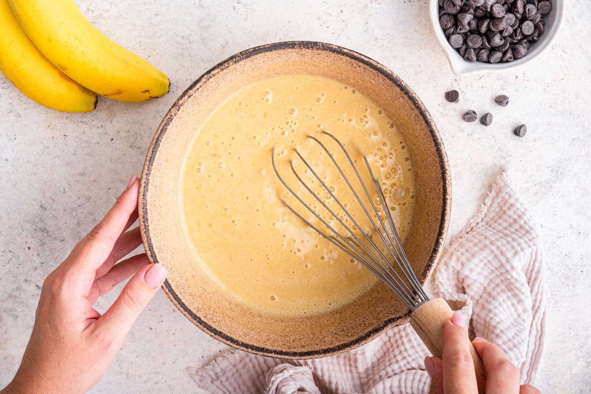 A woman's hand whisking the wet ingredients for the protein banana bread in a large mixing bowl.