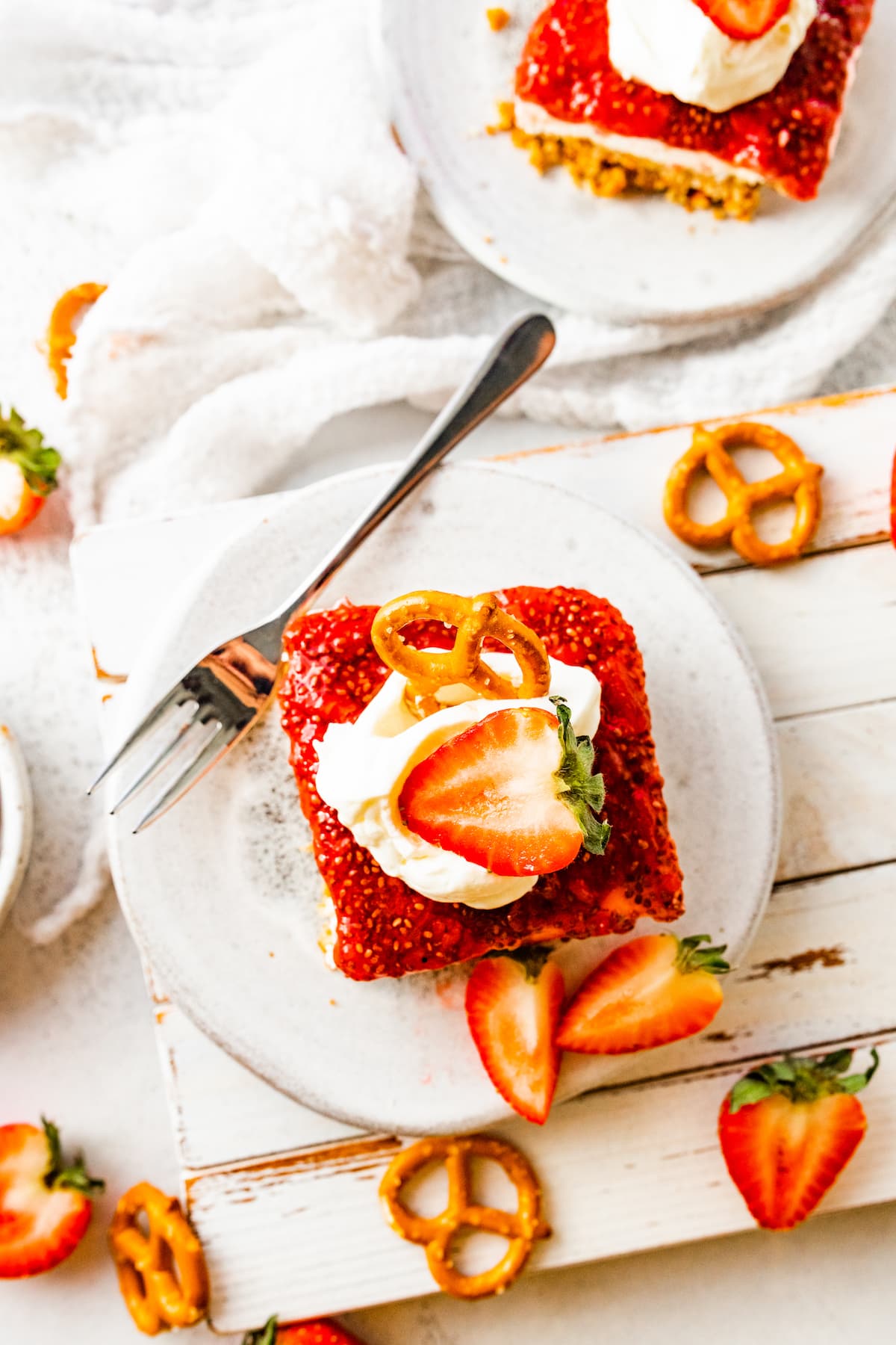 A slice of strawberry pretzel cake on a small plate and topped with whipped cream.