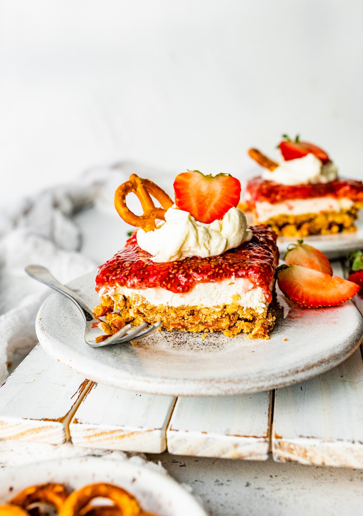 A slice of strawberry pretzel salad on a small plate with a whipped cream topping and sliced strawberries on the side.