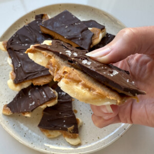 A woman's hand holding a piece of banana bark with layers of peanut butter and chocolate.