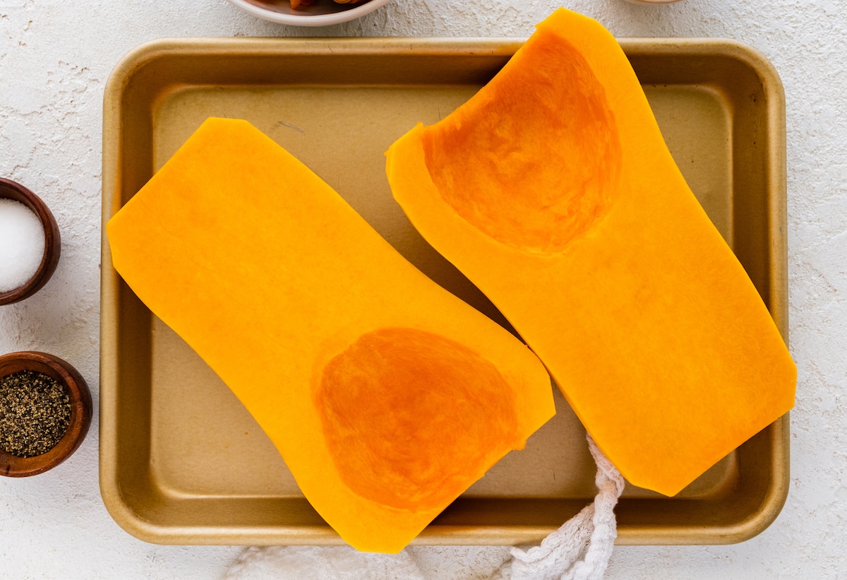 A butternut squash split in half on a baking tray.