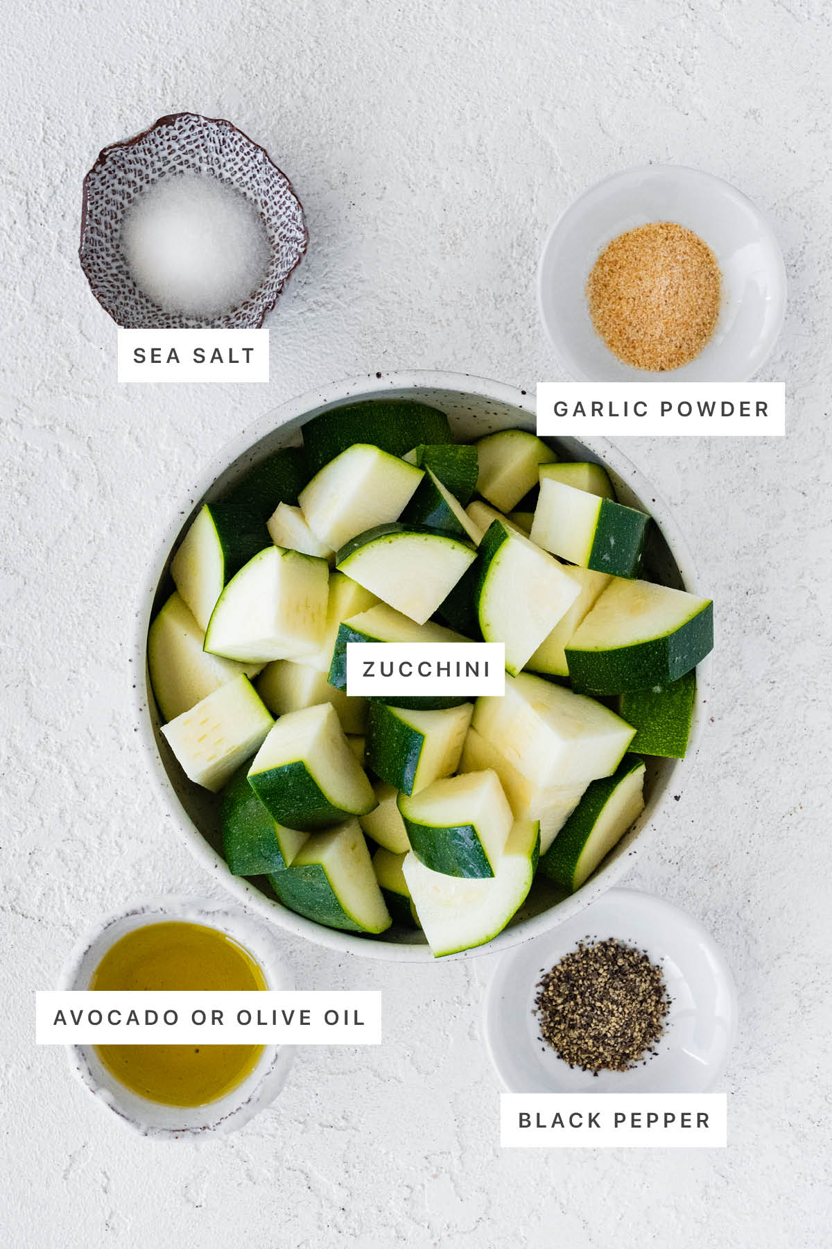 Ingredients measured out for Air Fryer Zucchini: sea salt, garlic powder, zucchini, olive oil and black pepper.