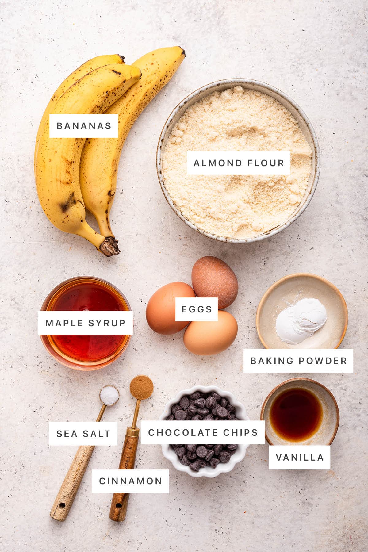 Ingredients measured out to make Almond Flour Banana Bread: bananas, almond flour, maple syrup, eggs, baking powder, sea salt, cinnamon, chocolate chips and vanilla.