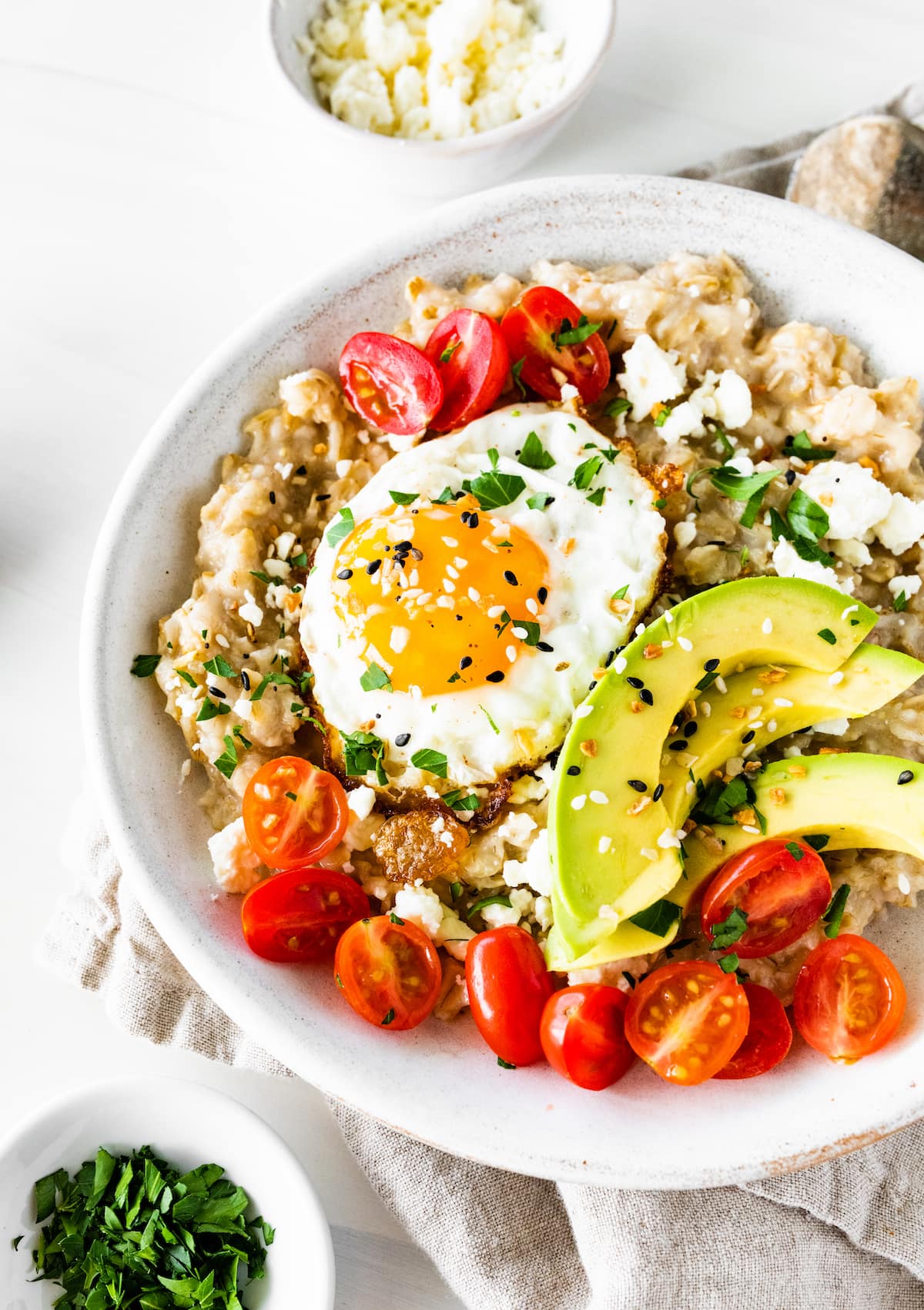 A bowl of oatmeal topped with cherry tomatoes, avocado slices, feta cheese, and a cooked egg.