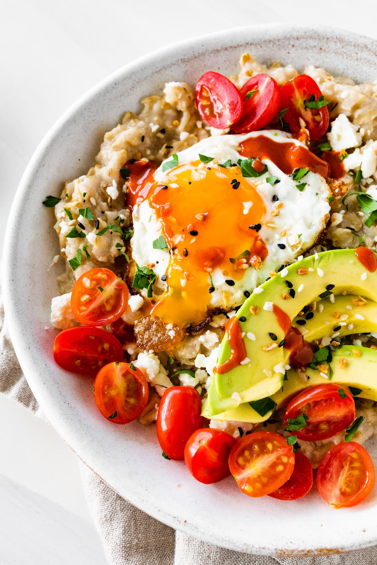 A serving of oatmeal topped with a cooked egg, avocado slices, cherry tomatoes, and sesame seeds.