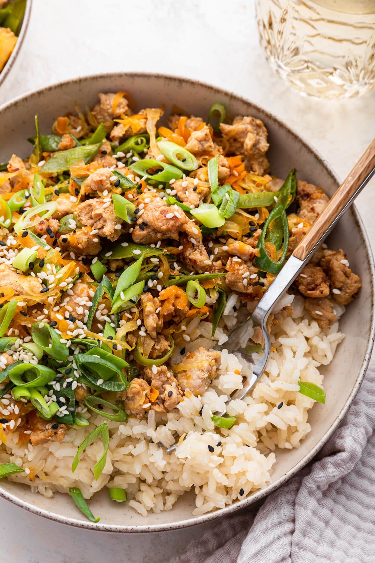 A serving of ground turkey in a bowl with white rice and garnished with green onion and sesame seeds.