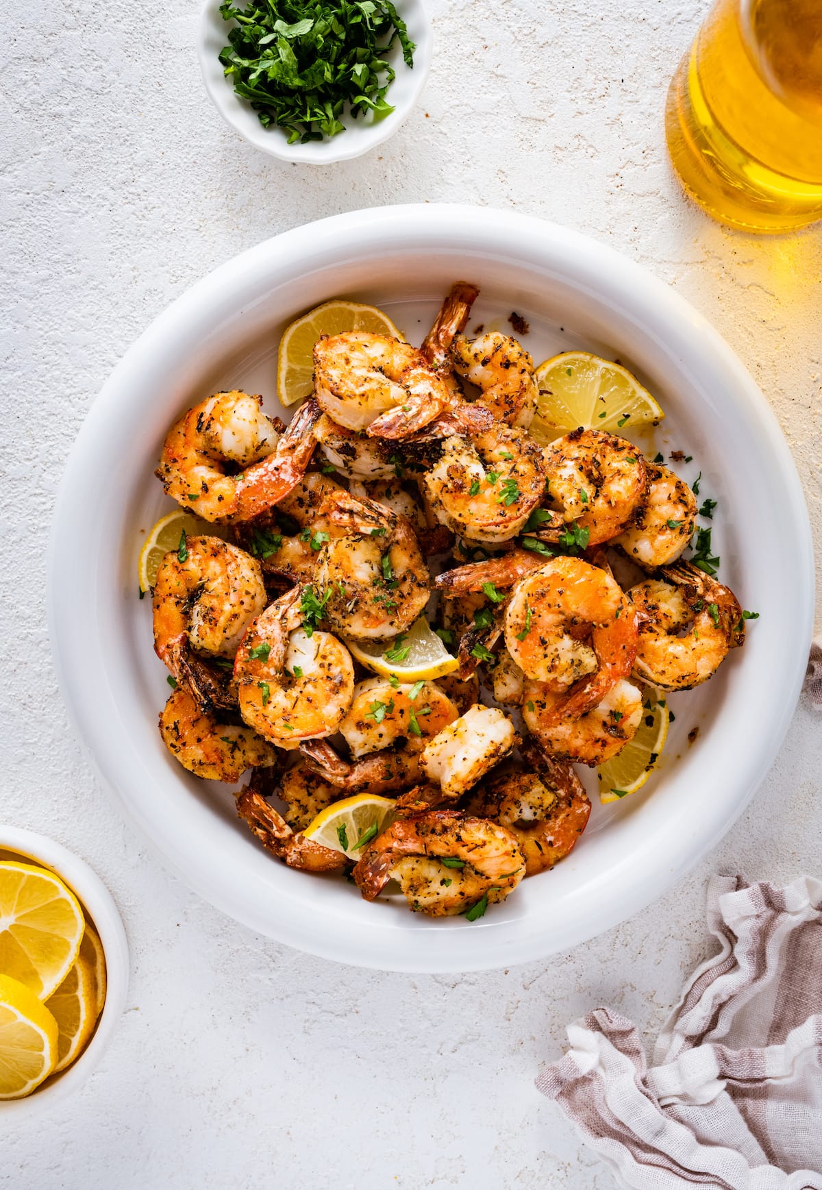 Seasoned air fried shrimp on a plate with lemon wedges.