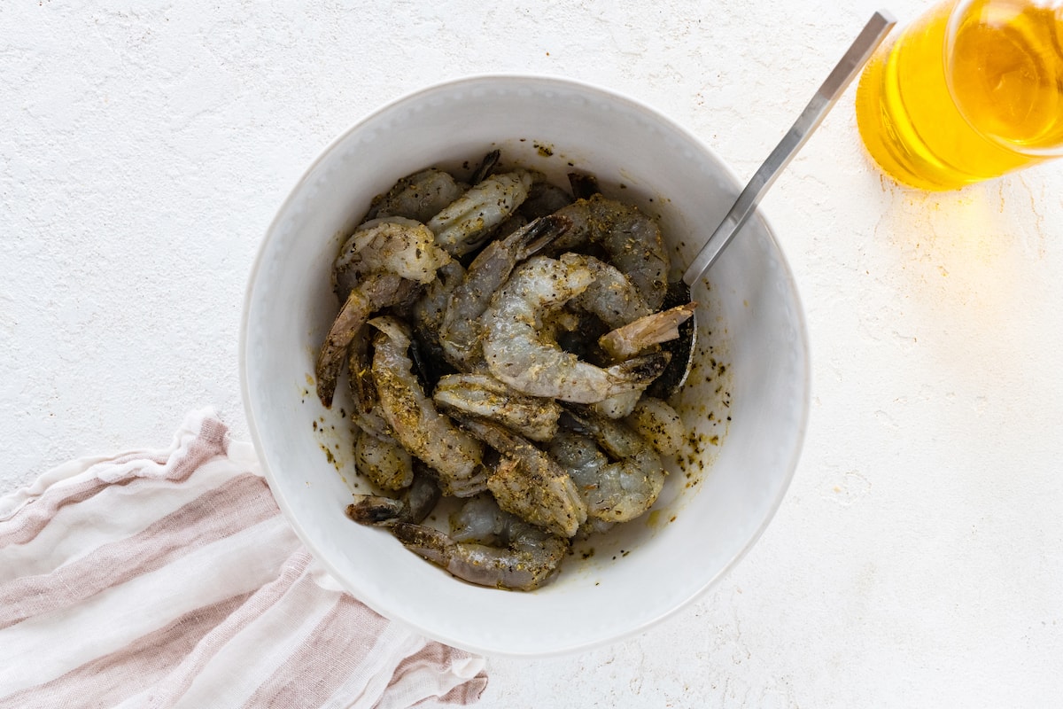 A large bowl with raw shrimp covered in olive oil, herbs, and spices.