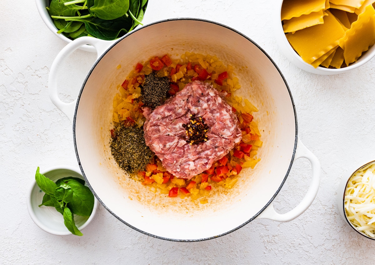 Ground pork sausage added with spices to a large pot of sautéed onions, red bell pepper, and garlic.