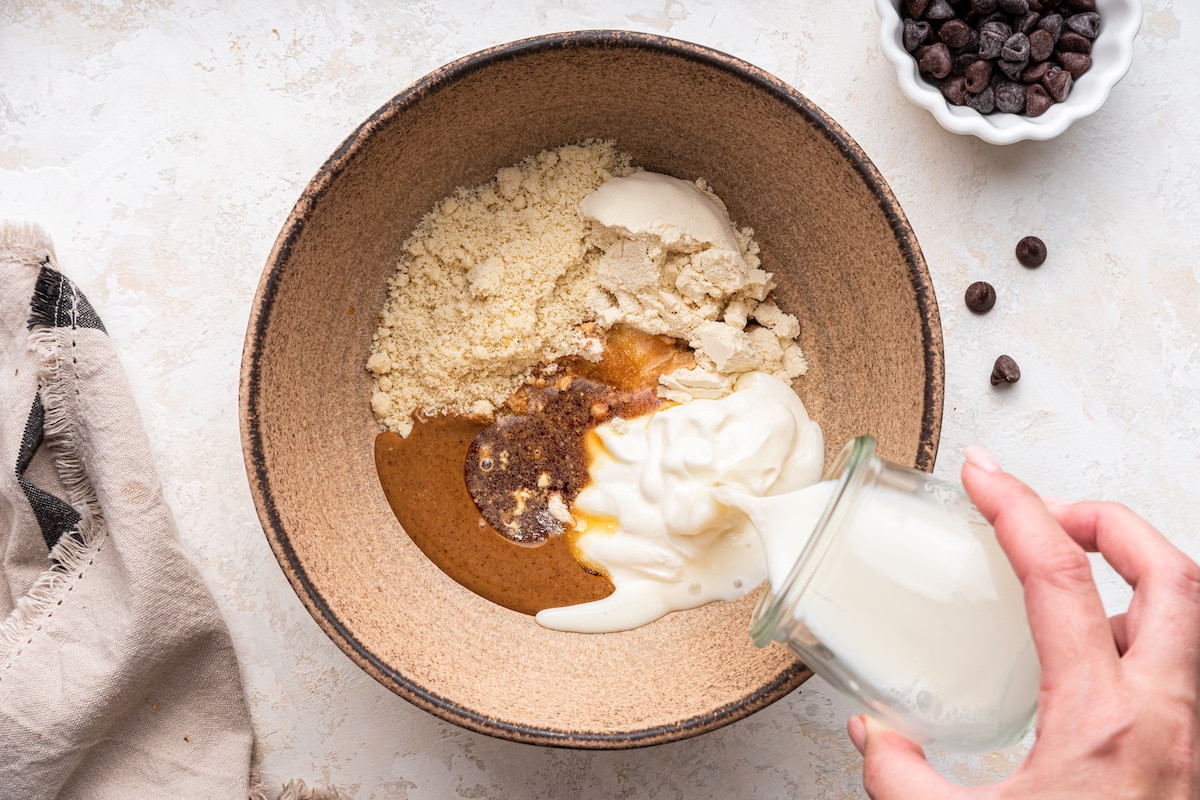 Milk being poured into a mixing bowl of ingredients to be used for a protein cookie dough.