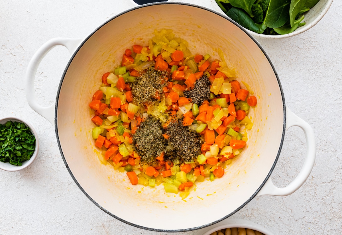 Sautéed vegetables in a large pot with added herbs and spices.