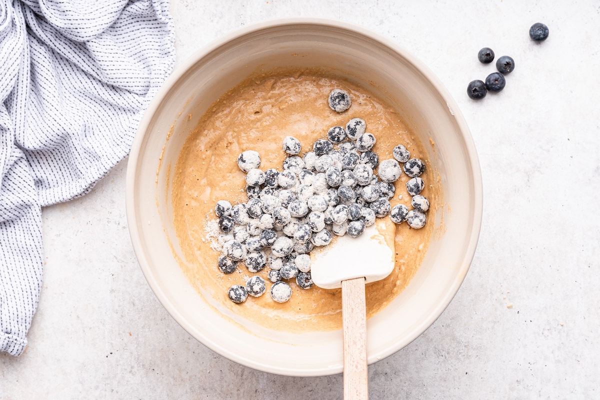 Frozen blueberries added to the batter used to make blueberry protein muffins.