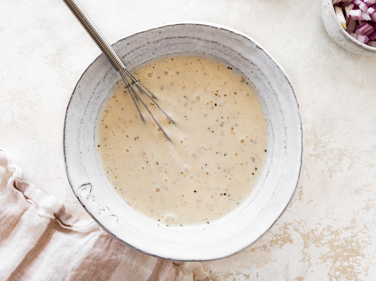 A dressing made with yogurt, vinegar, and spices in a small bowl with a metal whisk.