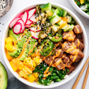 Finished poke bowl with all toppings - ahi tuna, jalapenos, cucumbers, radishes, avocado, mango, seaweed salad and scallions. Bowl is drizzled with sriracha mayo and topped with sesame seeds.