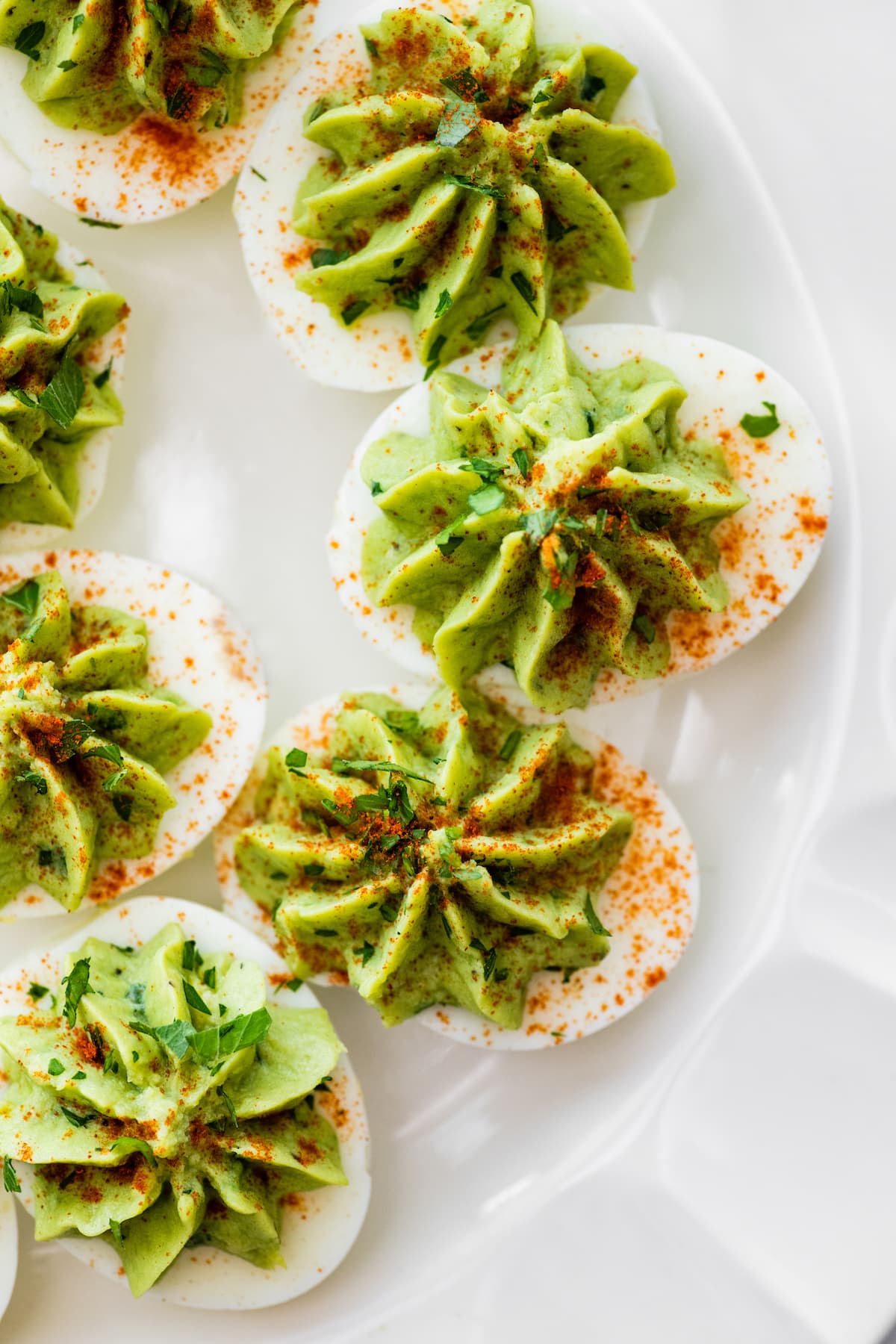 Avocado deviled eggs served on a plate and garnished with paprika and fresh herbs.