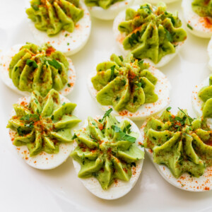 Avocado deviled eggs served on a plate topped with paprika, and fresh herbs.