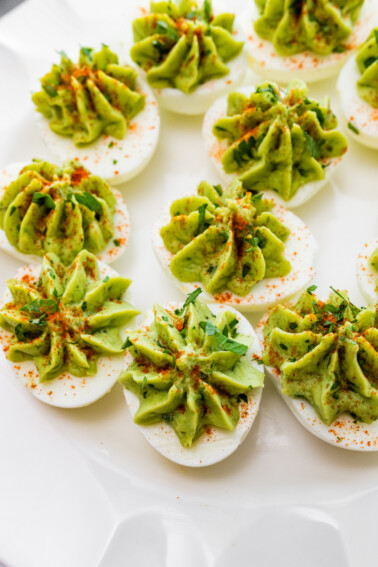 Avocado deviled eggs served on a plate topped with paprika, and fresh herbs.