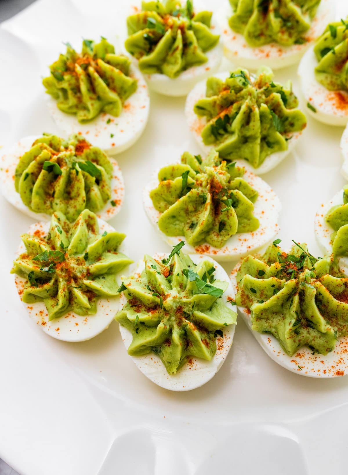 Avocado deviled eggs served on a plate topped with paprika, and fresh herbs.