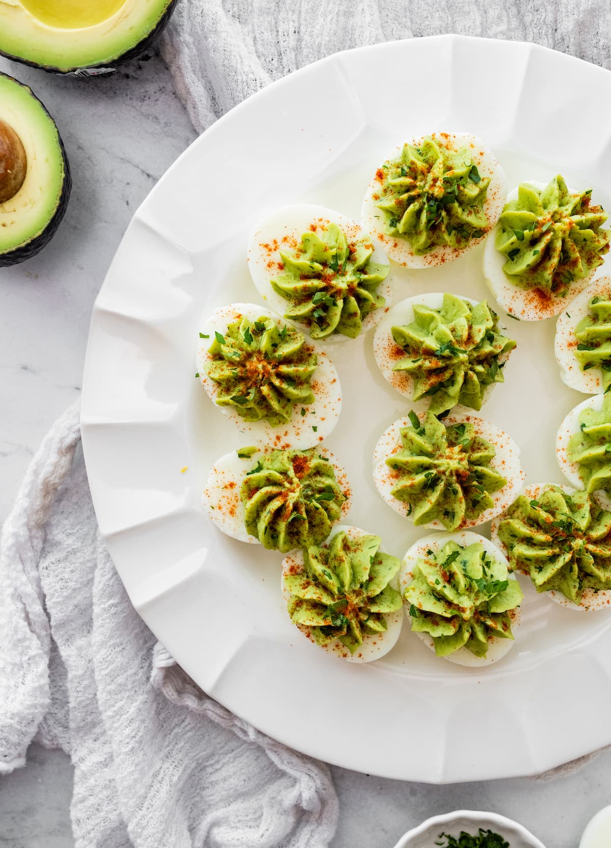 Avocado deviled eggs presented on a plate with a garnish of paprika and fresh herbs.