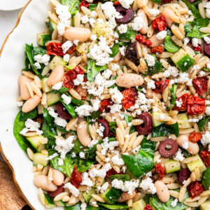 A large bowl of Mediterranean orzo salad with cooked beans, feta cheese, olives, sun dried tomatoes, and spinach.