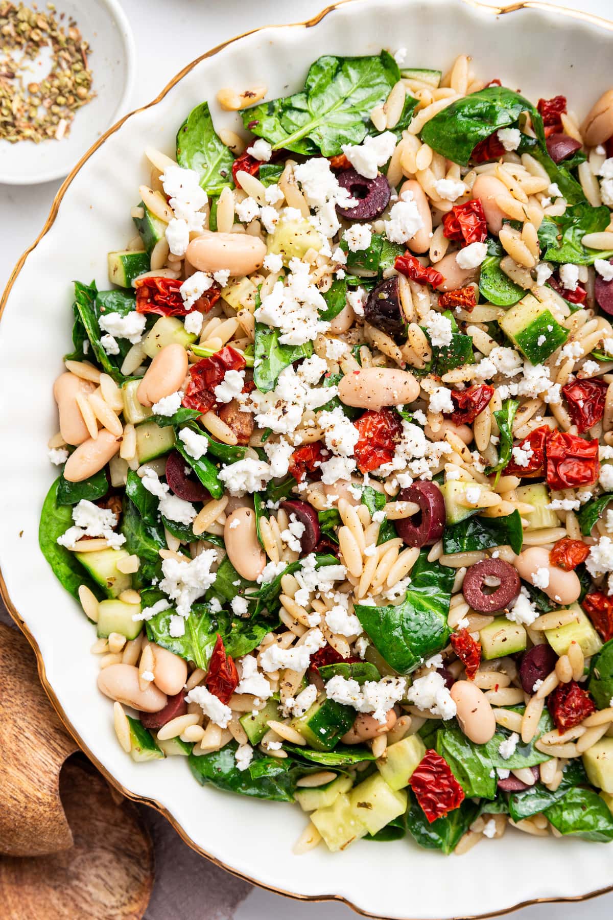 A large bowl of Mediterranean orzo salad with cooked beans, feta cheese, olives, sun dried tomatoes, and spinach.