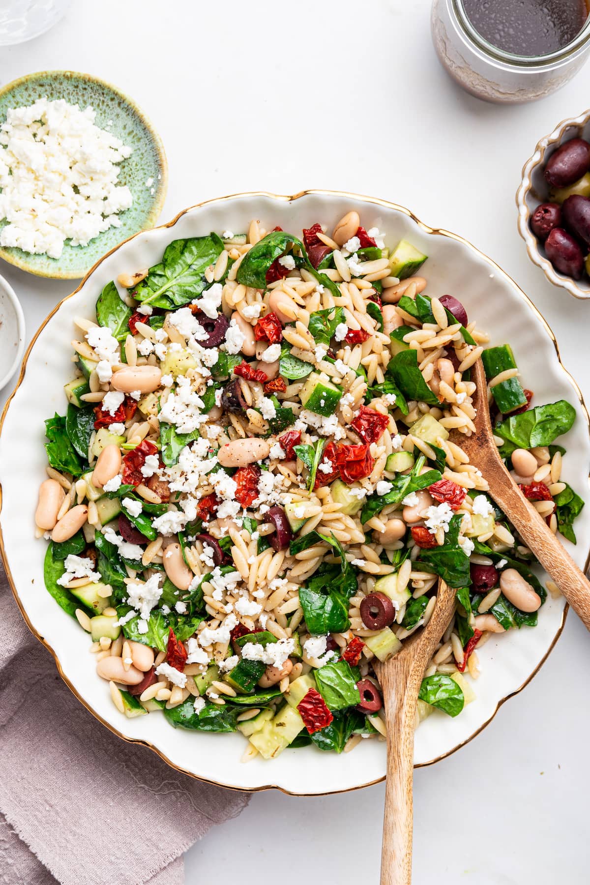 A large serving bowl of Mediterranean orzo salad with two wooden serving spoons.