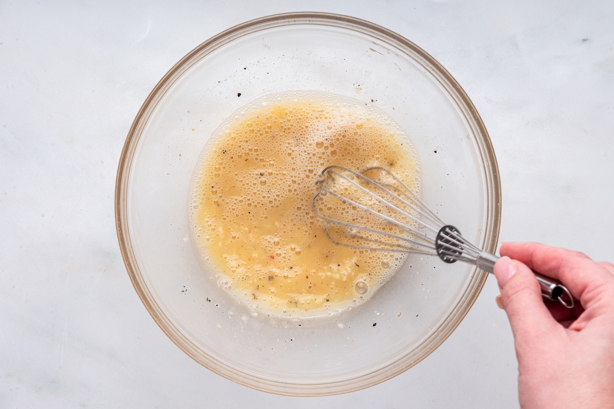 A woman's hand whisking together the marinade for the air fryer chicken cutlets.