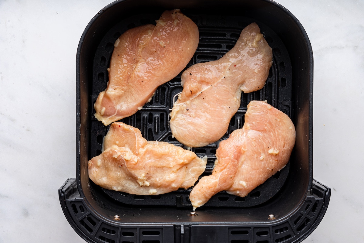 Four raw chicken cutlets in an air fryer basket.